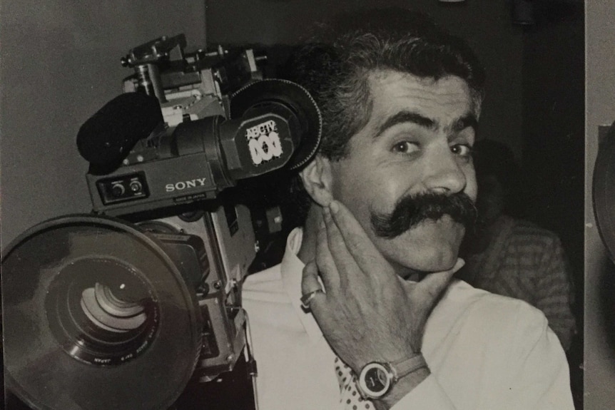 Black and white photo of Vince with big bushy moustache holding camera.