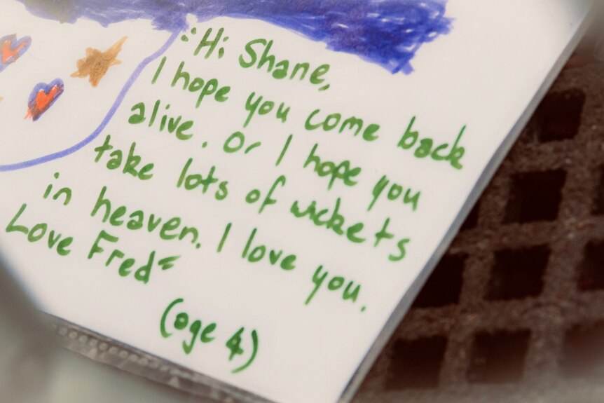 A close-up photo of a card dedicated to Shane Warne which says 'I hope you take lots of wickets in heaven'.