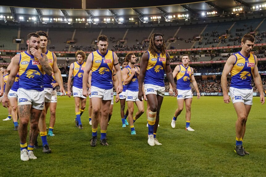A dejected footy team walks off the ground.