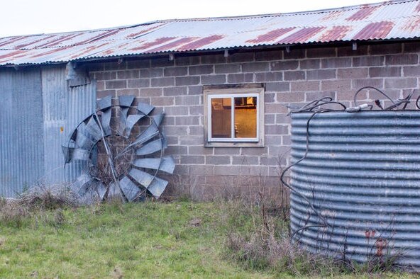An old farm building, with a corrugated iron tank, and windmill.