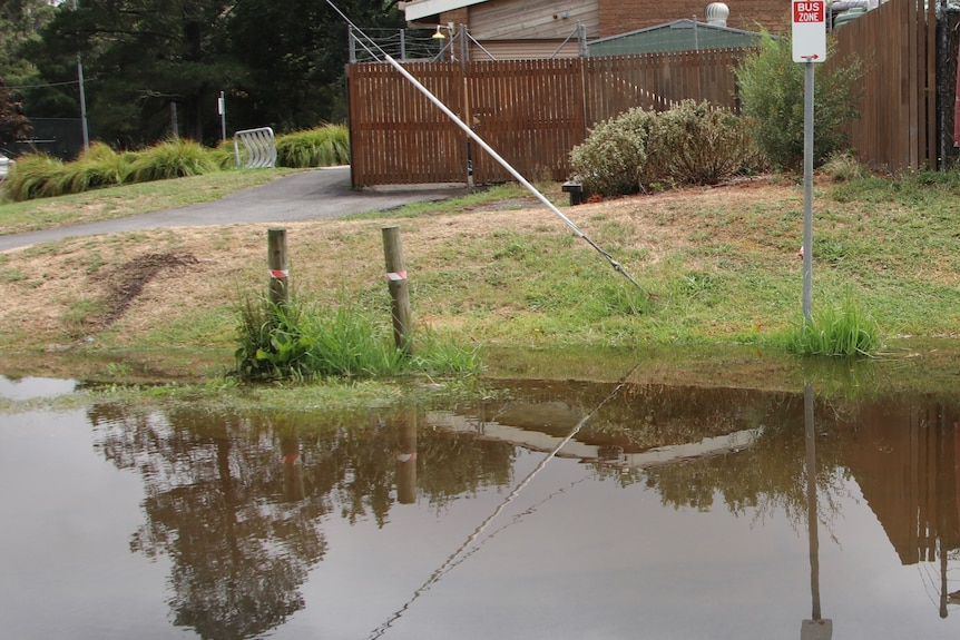 A road with floodwater on the side, with a country house in the background.