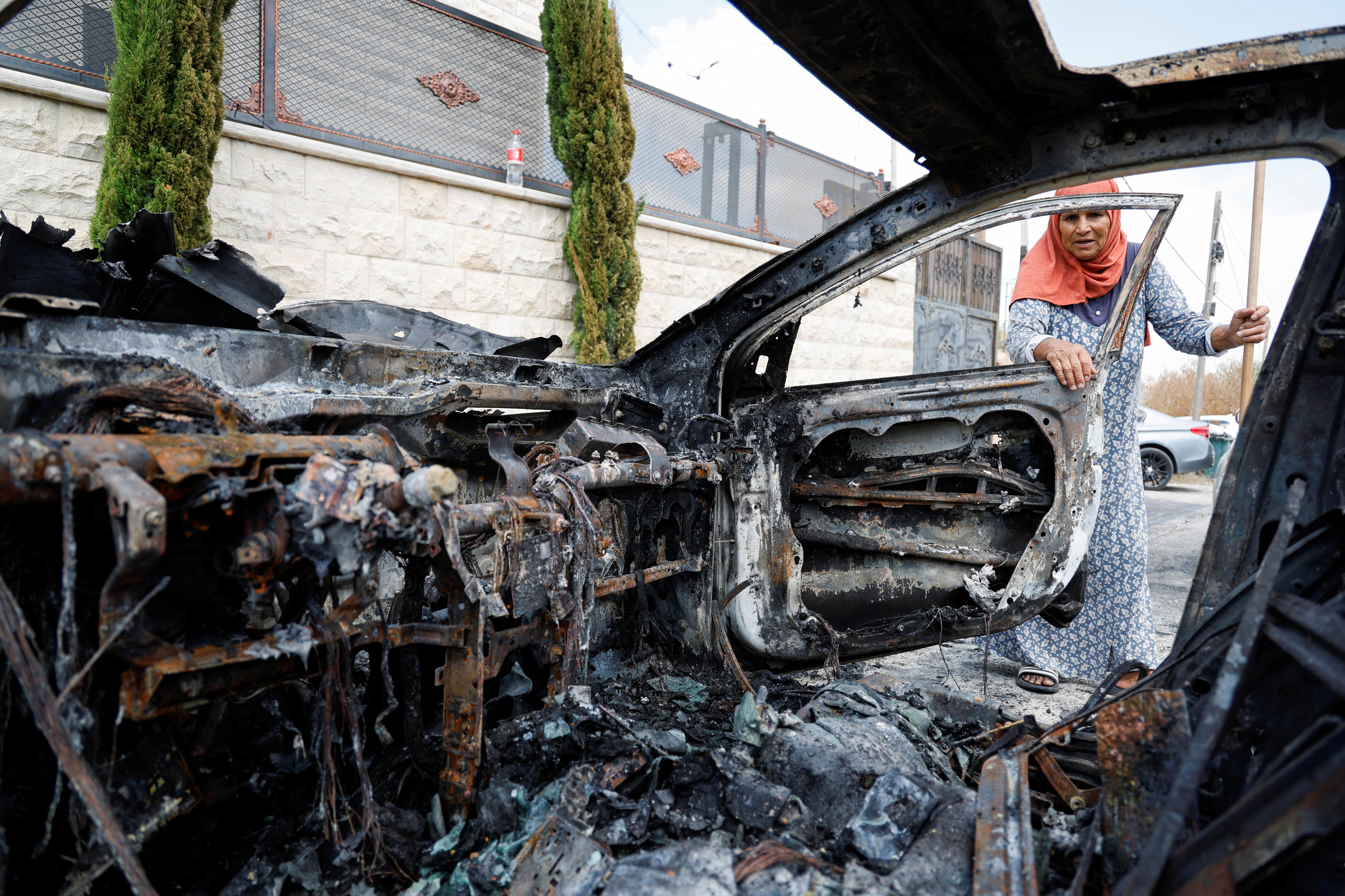 A woman looks into a burnt-out car.