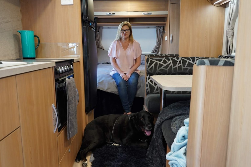Robyn Cairns sitts on bed on caravan with pet dog