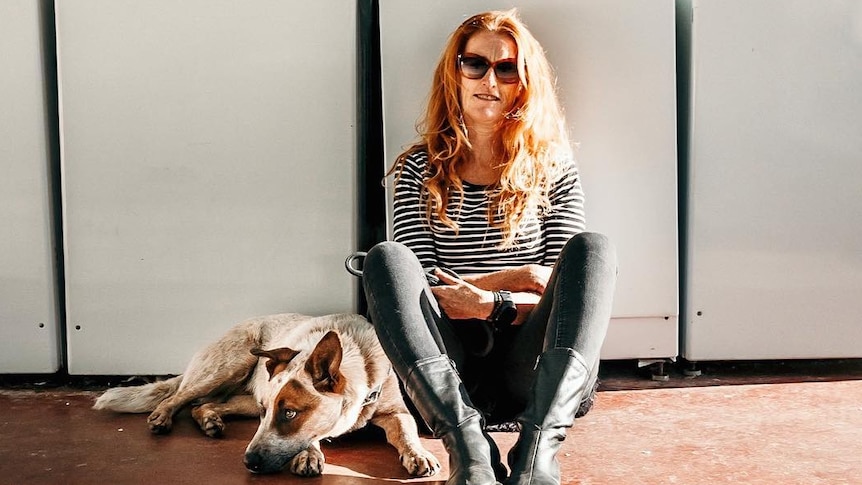 A woman and dog sit in front of a washing machine.