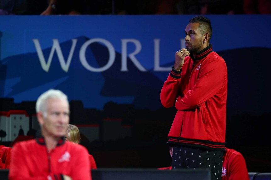A pensive tennis player watches a match from the sidelines during a teams event.