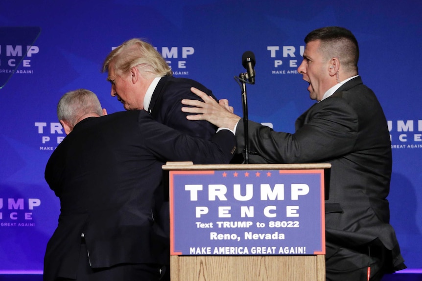 A group of Secret Service agents escort Trump off the stage.