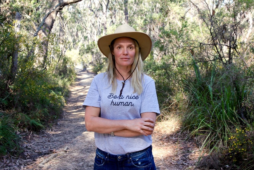 A woman, Christie Little, stands on a trail in a forest