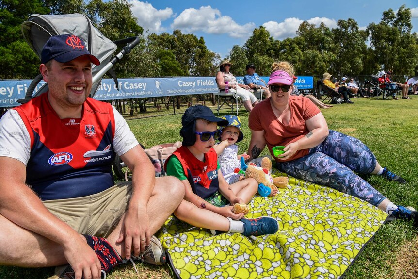A family sits on a rug on a hill watching the AFLW.