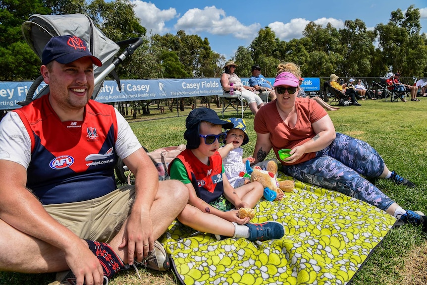 A family sits on a rug on a hill watching the AFLW.