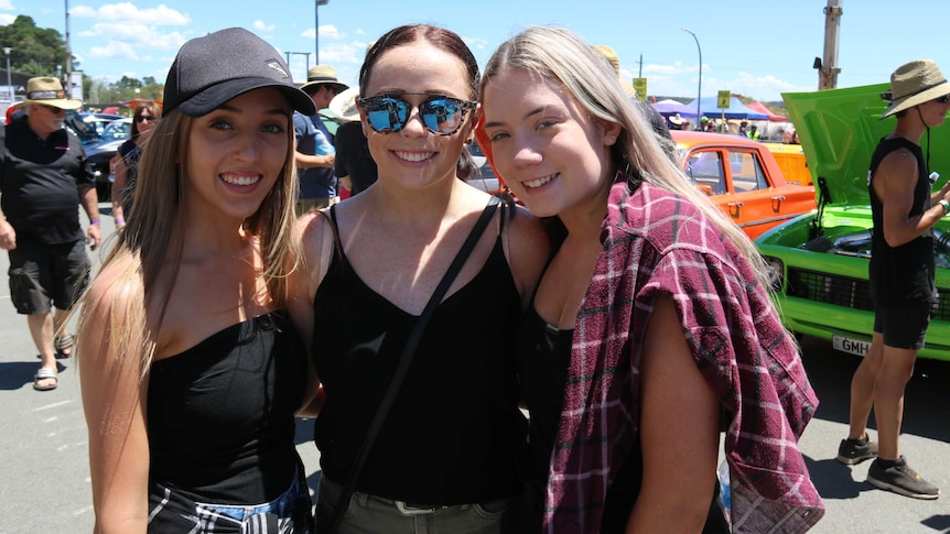 Three women stand in front of cars at Summernats.