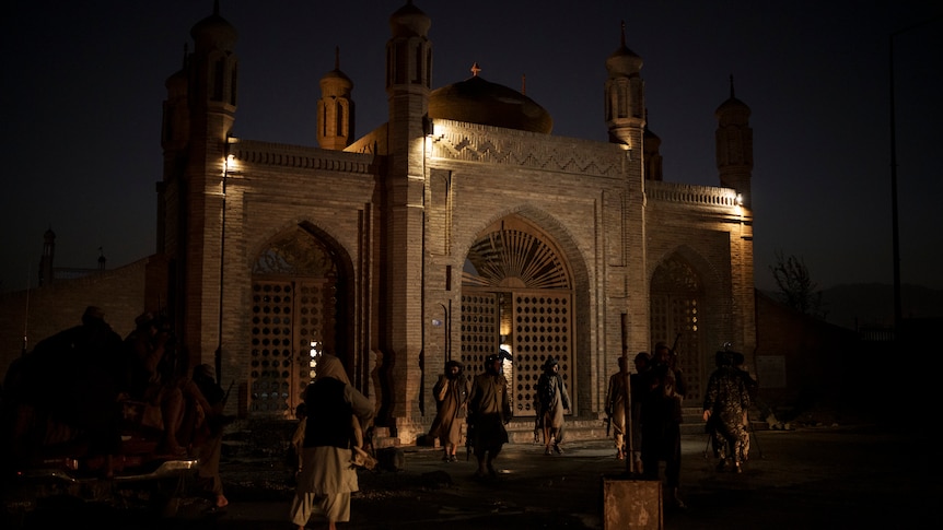 Taliban fighters walk at the entrance of a Kabul mosque at night