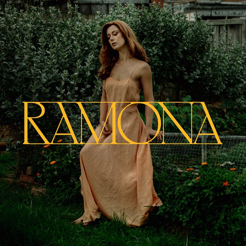 Artwork for Grace Cummings' 2024 album Ramona: stands in silk dress by a hedge with title embossed in gold