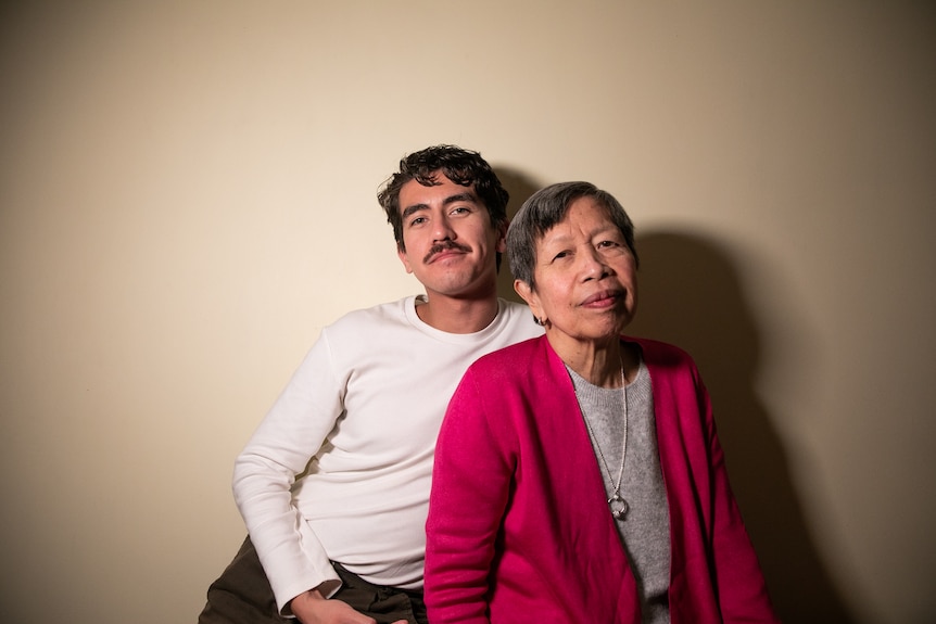 You view a 20-something Eurasian son pictured with his Filipina mother against a cream wall.