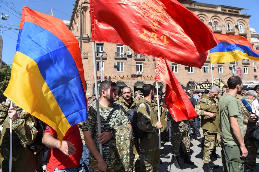 Men gather in the street wearing army camouflage and holding flags.