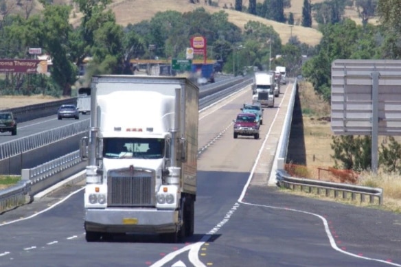 Trucks and cars travelling along a road, with rolling country hills in the background.