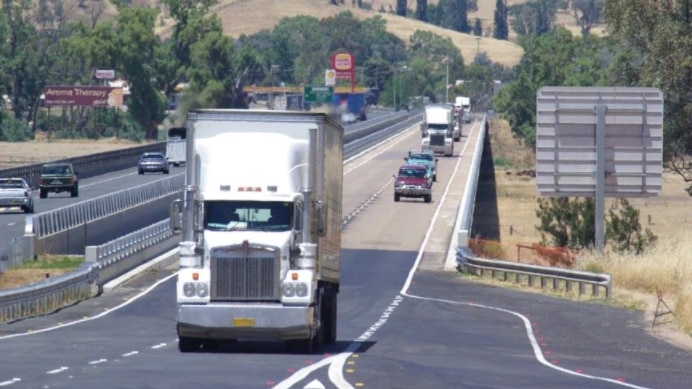 Trucks and cars travelling along a road, with rolling country hills in the background.