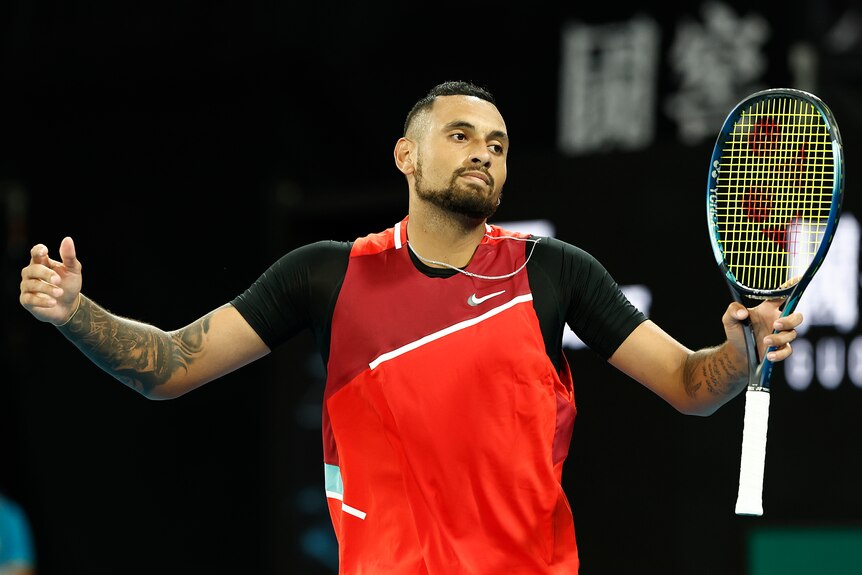 An Australian male tennis players stands holding his racquet with his arms outstretched.