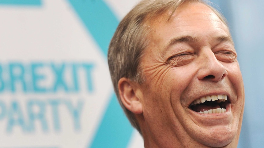 Nigel Farage laughs as he stands in front of the logo of his new political party