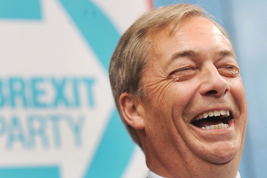 Nigel Farage laughs as he stands in front of the logo of his new political party