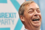 Nigel Farage laughs as he stands in front of the logo of his new political party