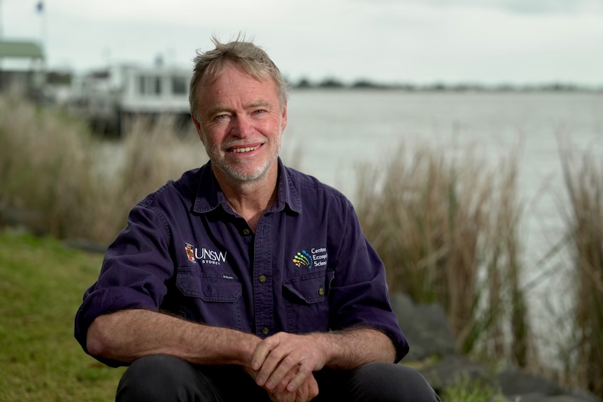 Man wearing a navy shirt sitting next to a river. 