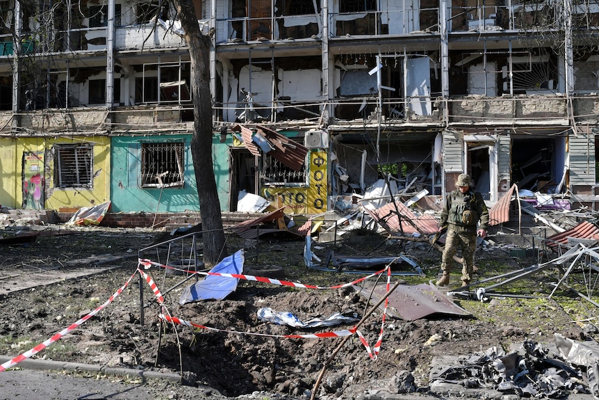 View of damaged apartment building and large hole in ground.