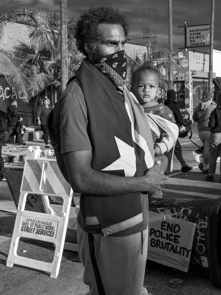 A man with a bandana shielding his face holds his son.