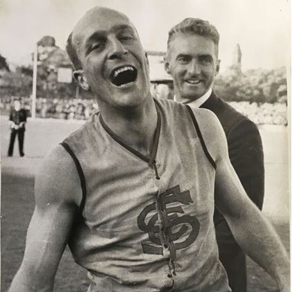 A SANFL footballer is pictured shouting in triumph as he stands next to an unnamed official after a grand final.