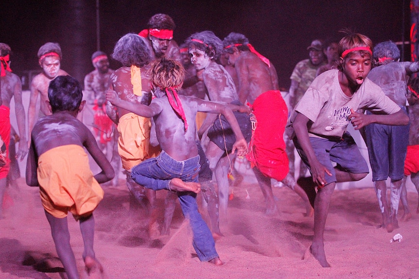 Indigenous children dancing in red dust at night.