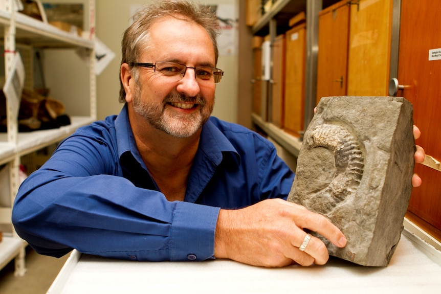 A man wearing a blue shirt holds a fossil