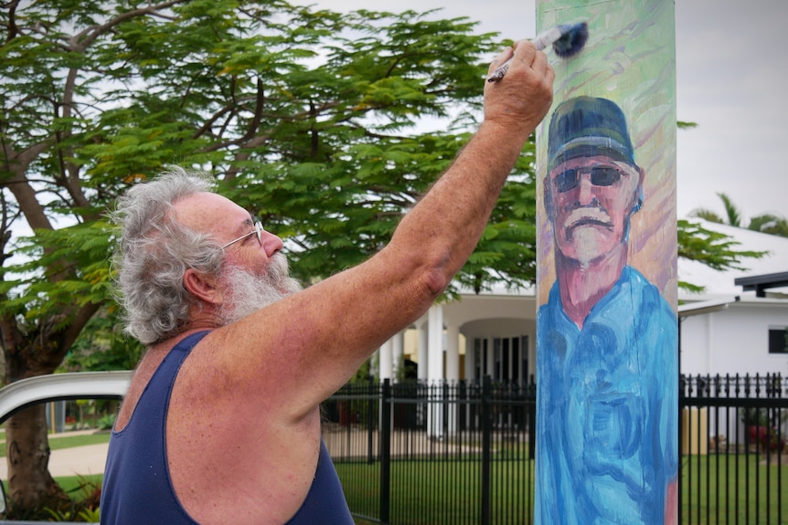 A man paints a portrait of a man on a power pole