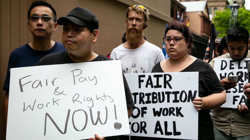 People hold placards that read: "Fair pay and work rights now".