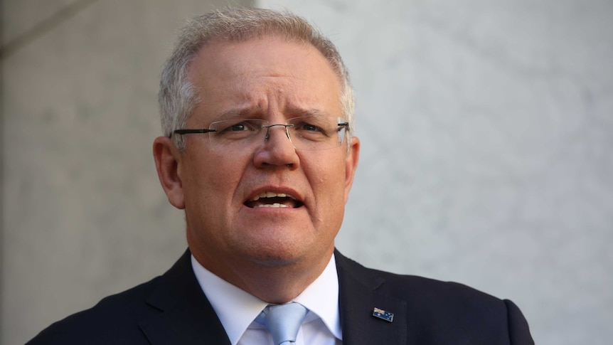 Close up of the Prime Minister mid-sentence wearing a suit with a blue tie and an Australian flag lapel pin.