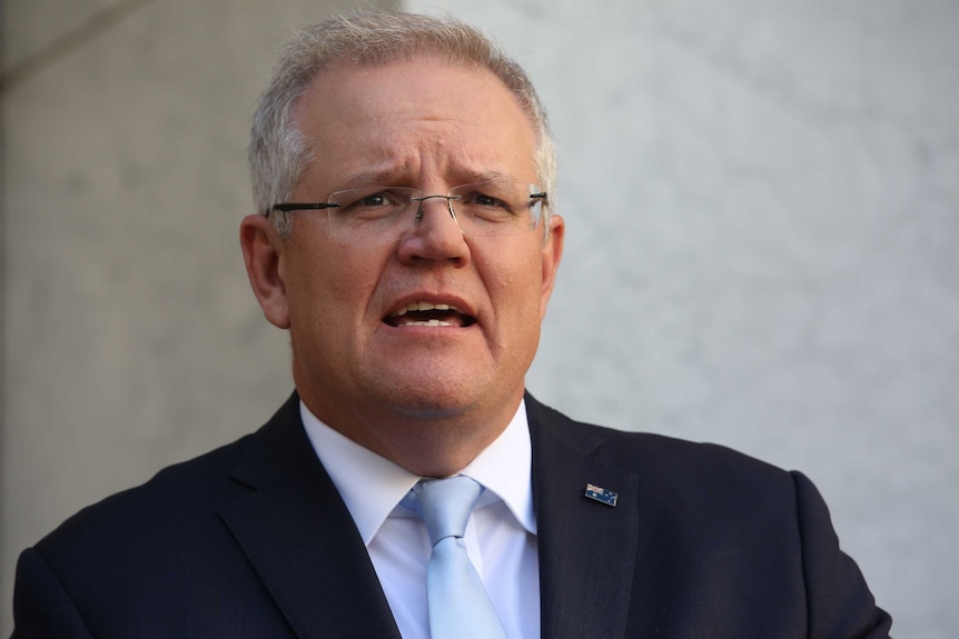 Close up of the Prime Minister mid-sentence wearing a suit with a blue tie and an Australian flag lapel pin.