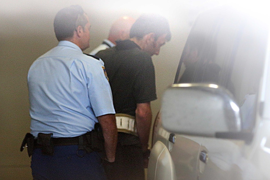 Mark Stocco is escorted by high risk transfer officers to a vehicle in Dubbo police station