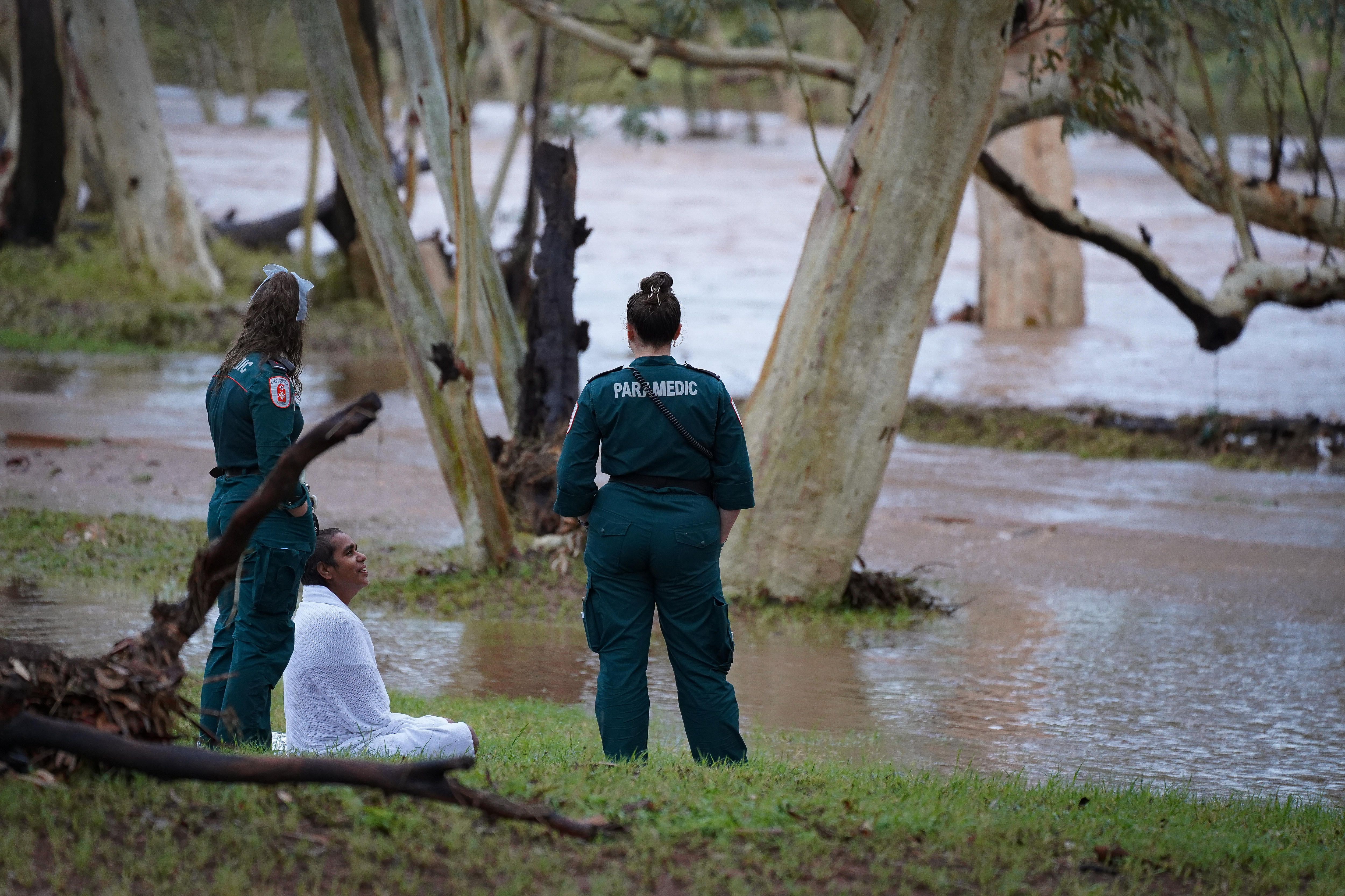 Dois paramédicos à beira do rio e uma mulher enrolada num cobertor. 