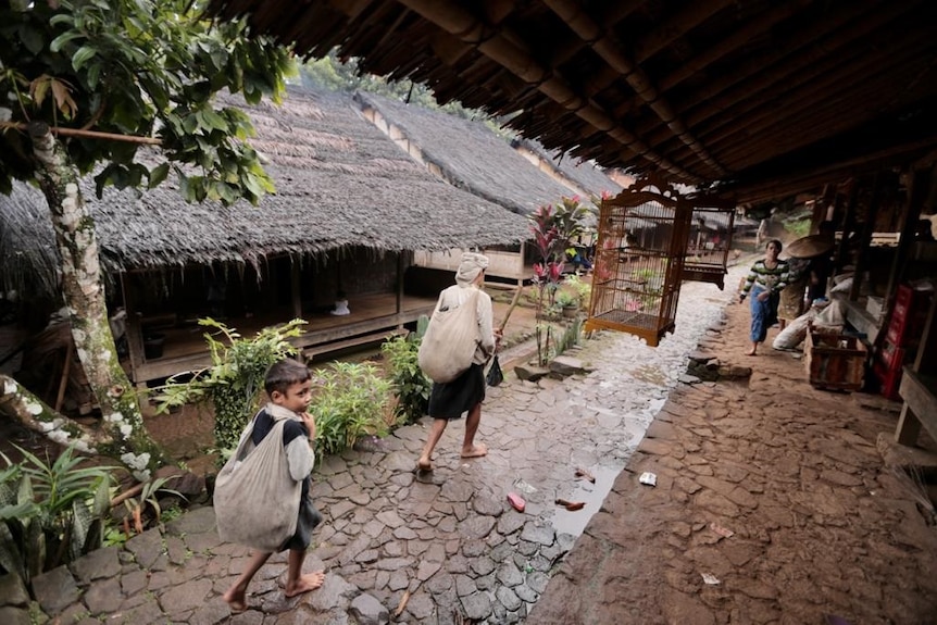 A man and a kid behind him walk in a pathway outside traditional houses.