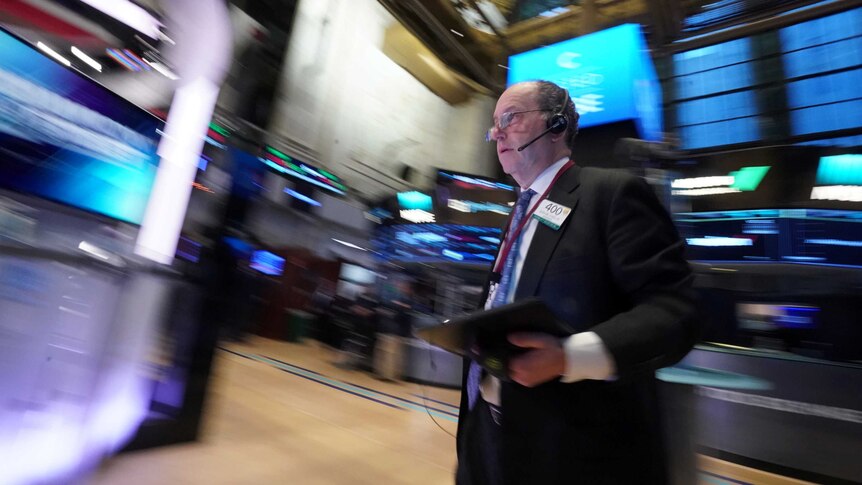 A man with glasses looks at a screen displaying financial information