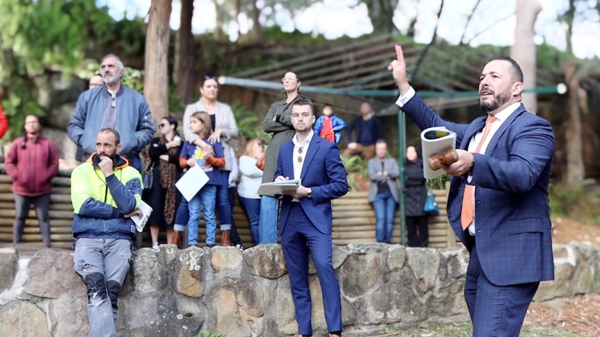 Un commissaire-priseur de Sydney tient un marteau alors qu'il encourage les offres de la foule.