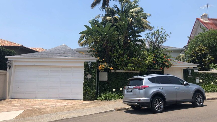 A car is parked outside a nice house with palm trees and a blue sky