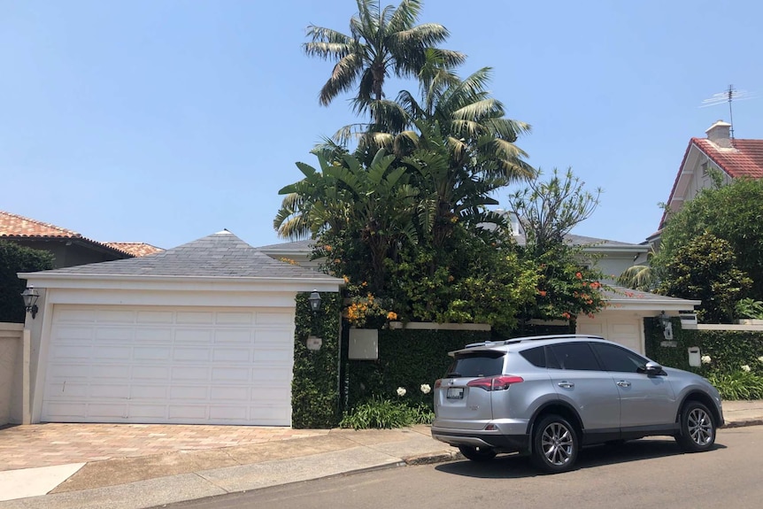 A car is parked outside a nice house with palm trees and a blue sky