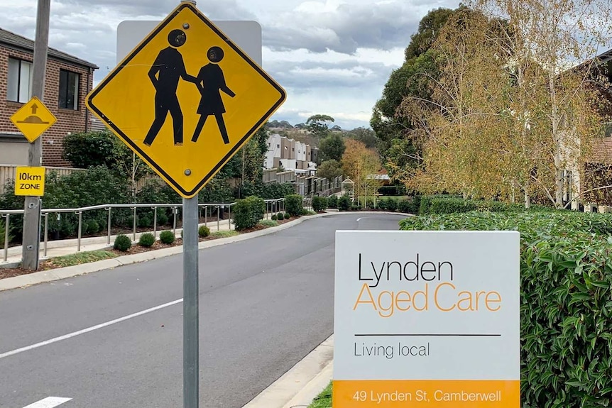 The driveway to an aged care village with the sign Lynden Aged Care at the entry in white, black and yellow.