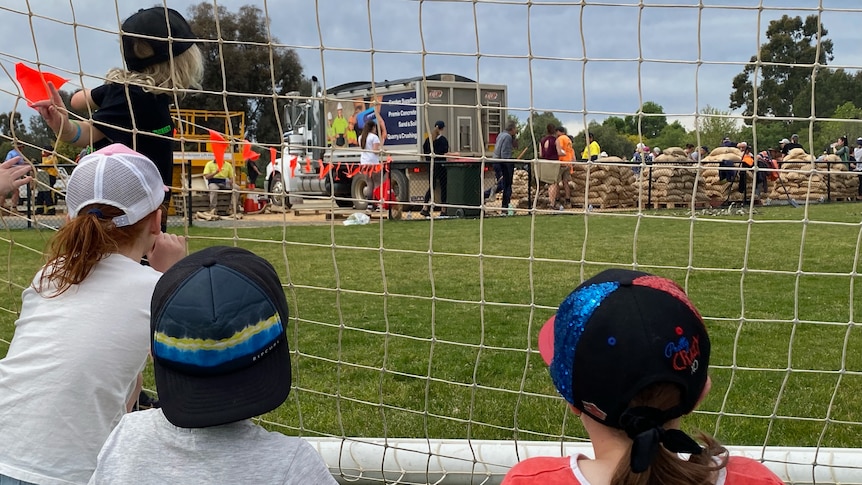 Children looking through the net of a soccer goal at sandbagging.