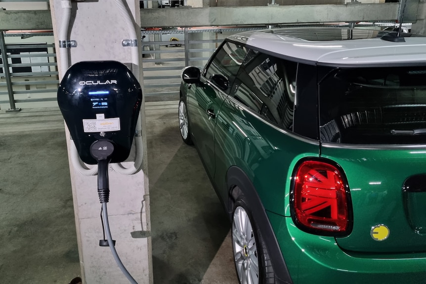 A small green electric car connected to a charger on a pillar in an underground carpark.