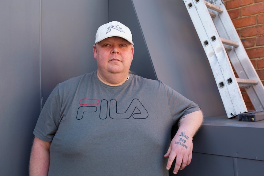 A man wearing a T-shirt and a cap looks at the camera.