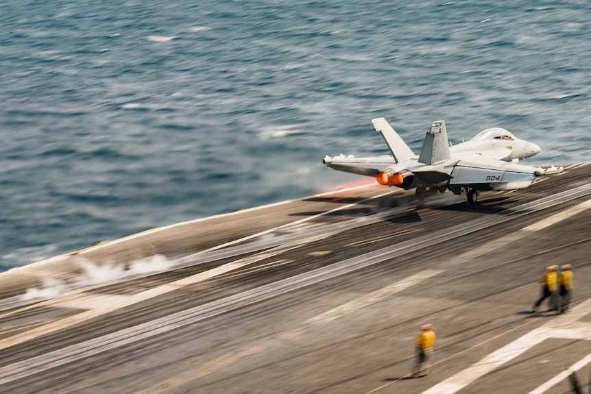 A US military jet is pictured mid-motion as it leaves the flight deck of an aircraft carrier.