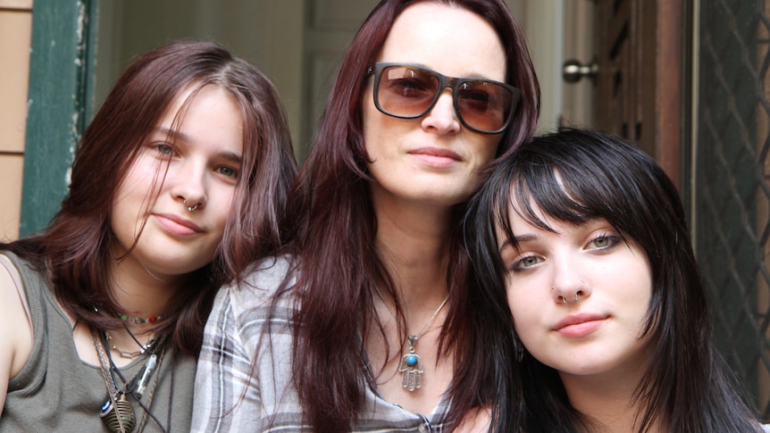 A portrait of Nicola and their two teenage daughters, sitting closely together and looking thoughtful.