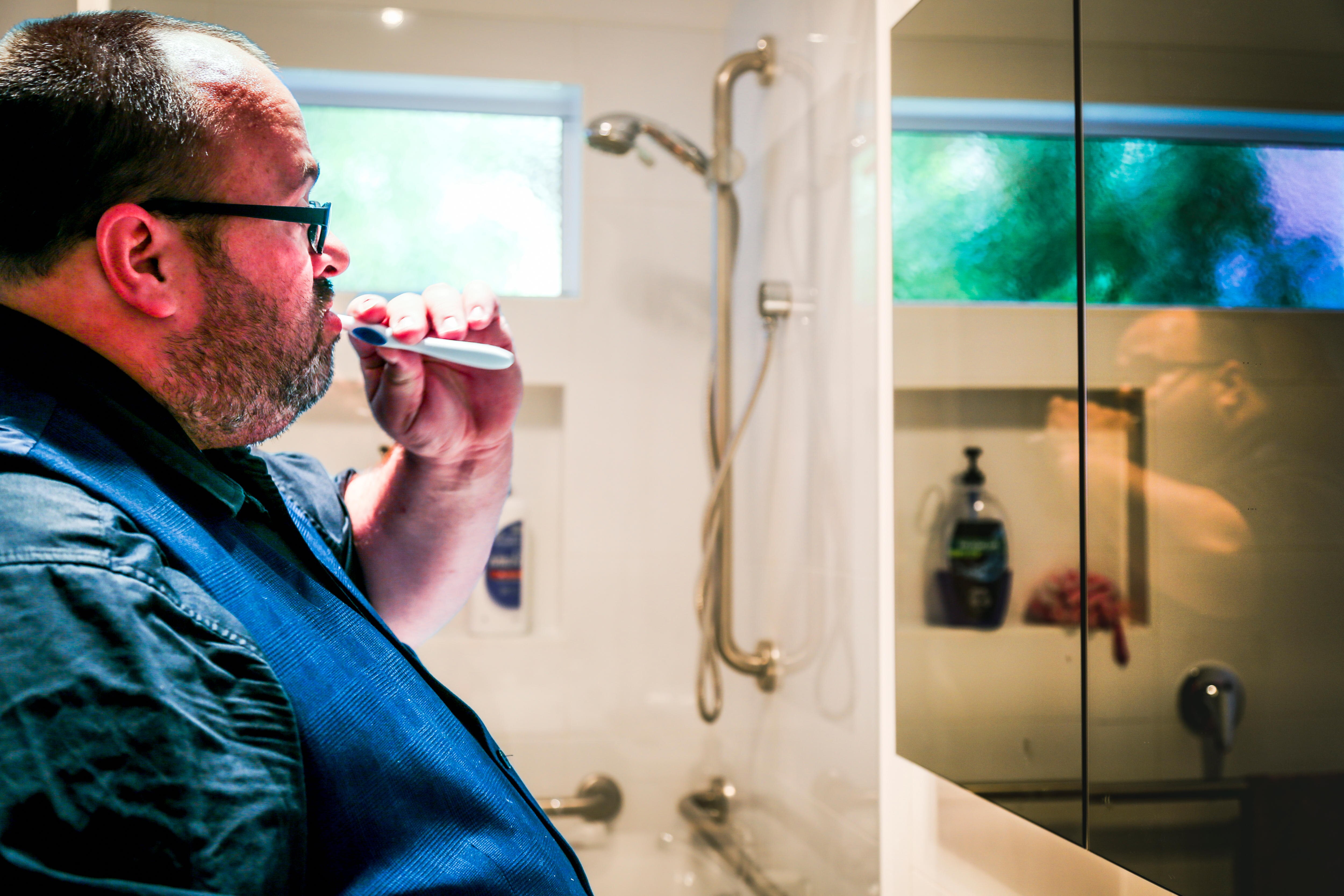 Cameron Bloomfield brushes his teeth while looking in the mirror, with his reflection looking back at him.