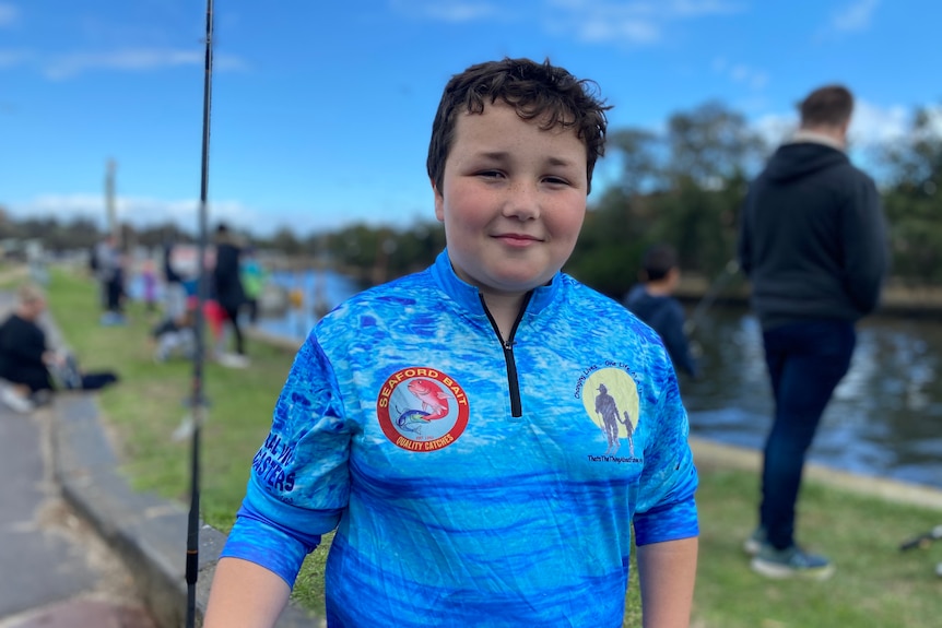 A boy with brown hair wearing a blue shirt and holding a fishing rod.