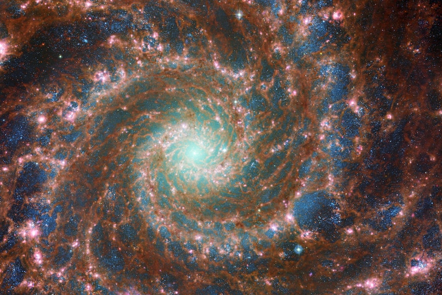 Spiralny obraz galaktyki.  Ciemnozłota gwiazda i gromady pyłu wydają się prawie splecione z ciemnoniebieskim kolorem przestrzeni
